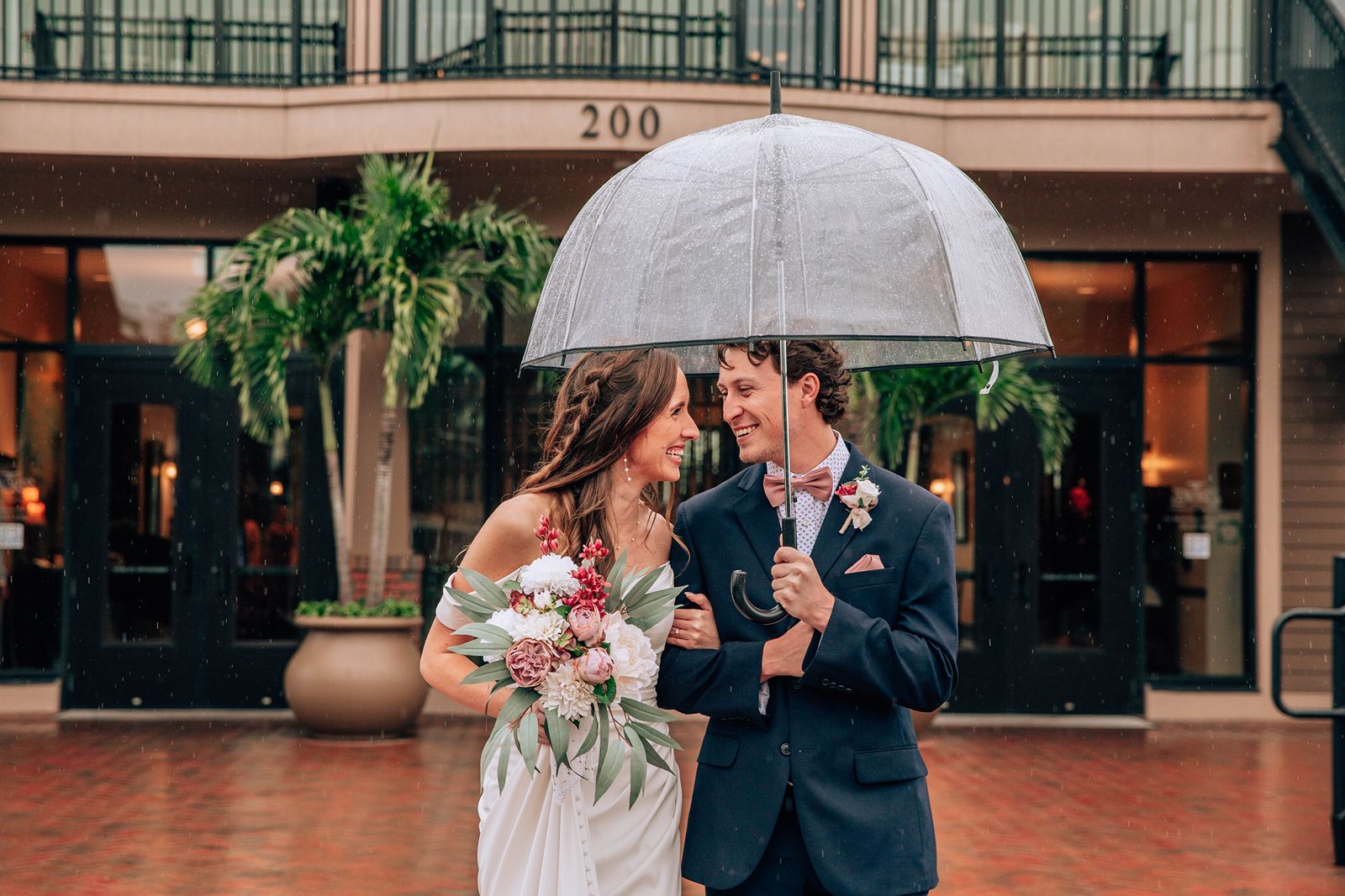 bride and groom walking under umbrella in the rain at tavares pavilion