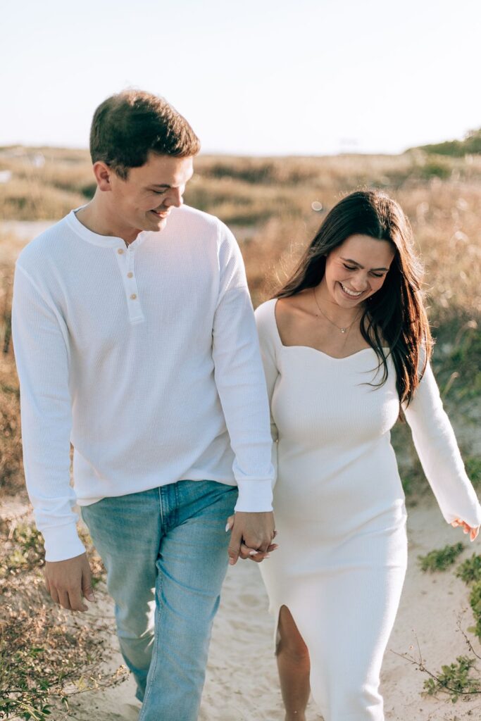 candid photo of bride and groom walking through sand dunes and smiling