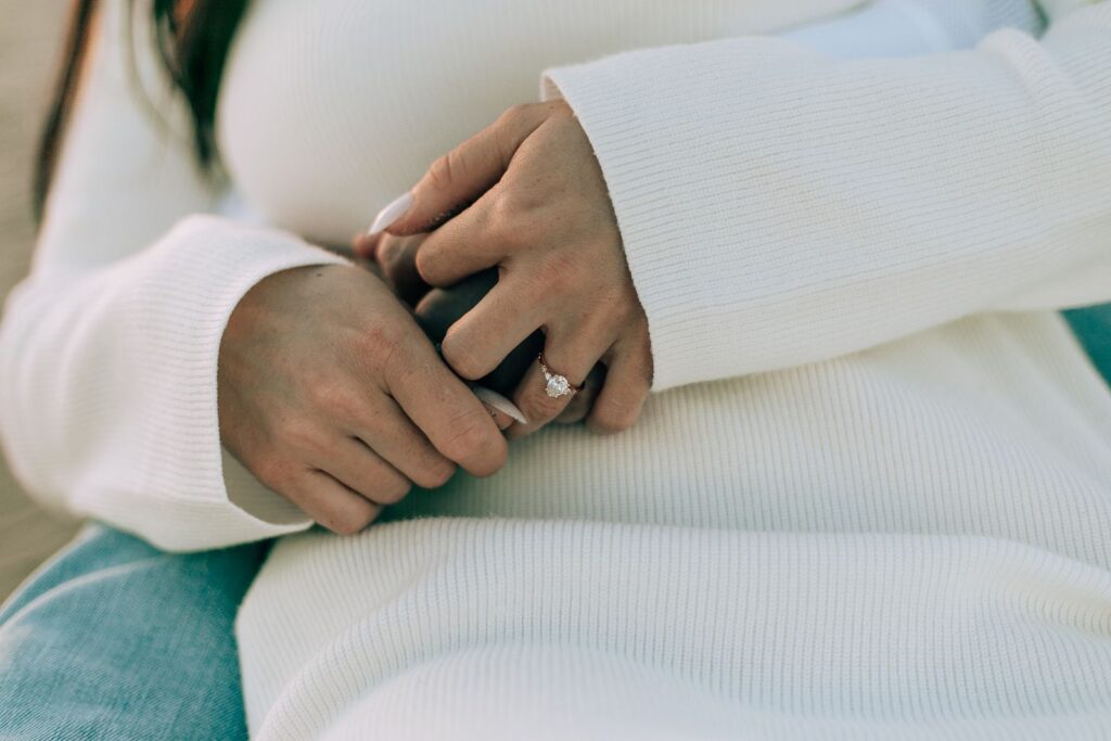 detail photo of the brides engagement ring as their arms and hands are wrapped up together on the beach