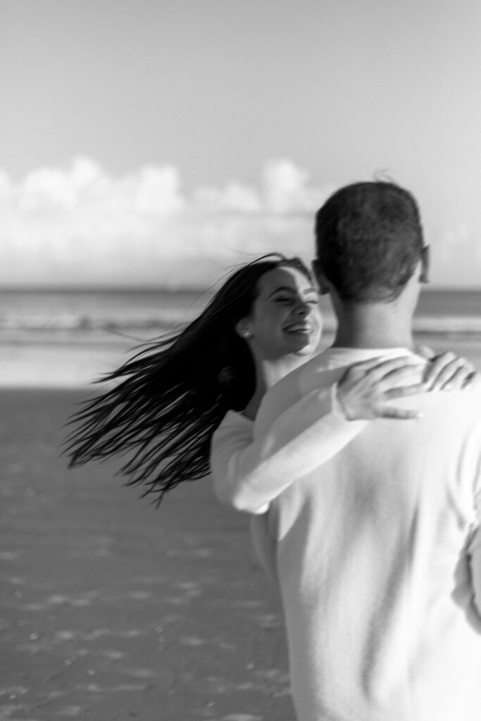 groom spins his fiance at the beach and her hair flows in the wind